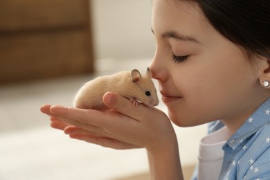 Little girl holding cute hamster at home, closeup