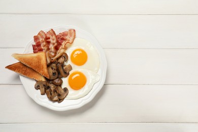 Plate of fried eggs, mushrooms, bacon and toasted bread on white wooden table, top view with space for text. Traditional English breakfast