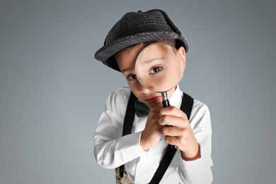 Little boy with magnifying glass playing detective on grey background