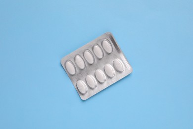 Photo of White pills in blister on light blue background, top view