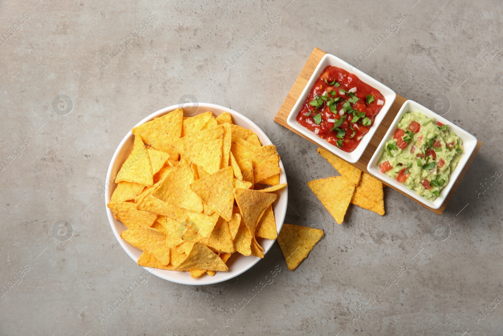 Photo of Bowl of delicious mexican nachos chips served with sauces on grey table, flat lay