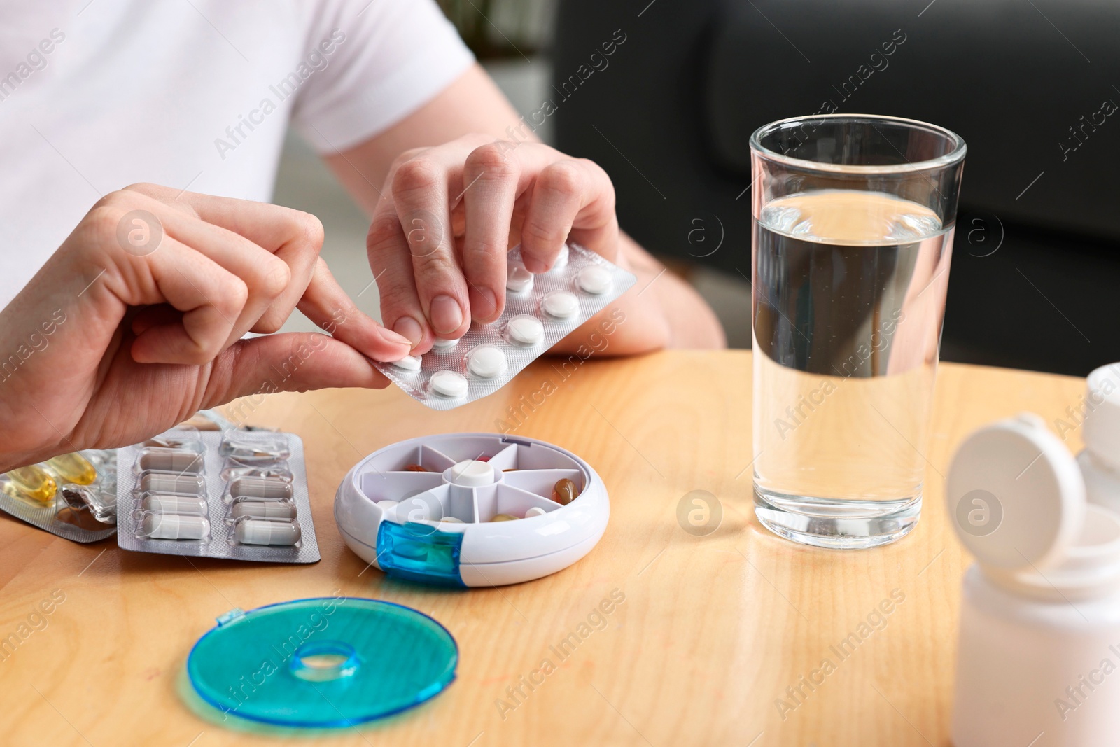 Photo of Woman with pills, organizer and glass of water at light wooden table, closeup