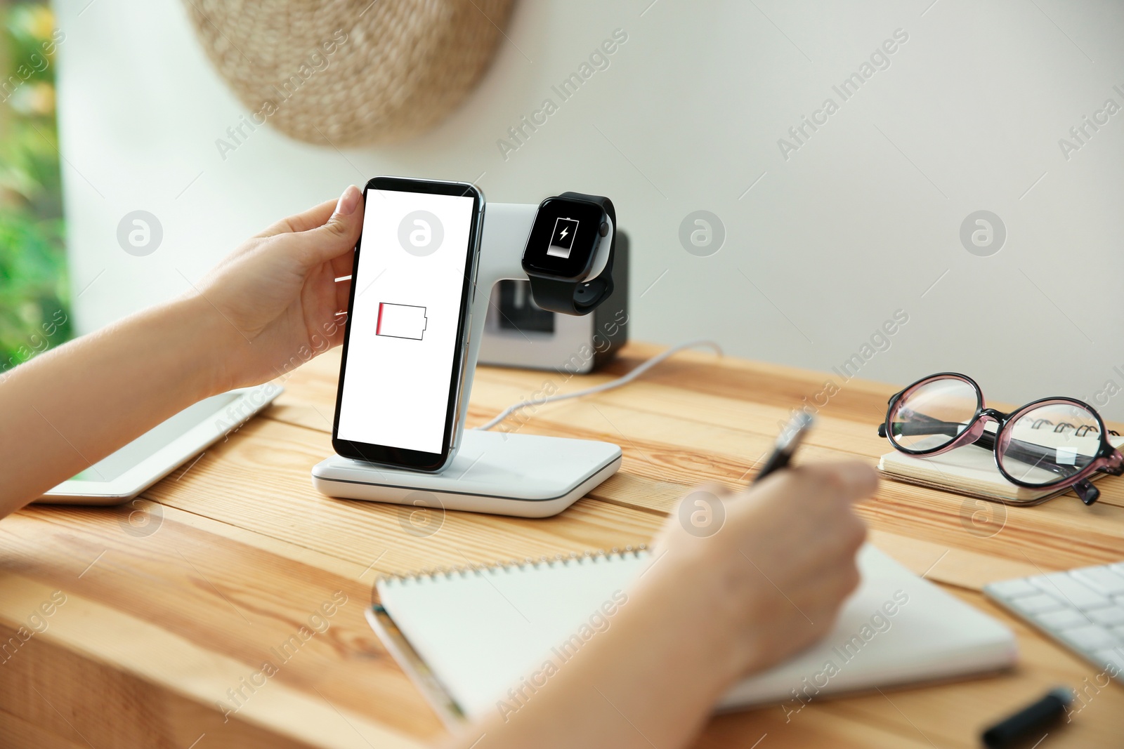 Photo of Woman putting mobile phone onto wireless charger at wooden table, closeup. Modern workplace accessory