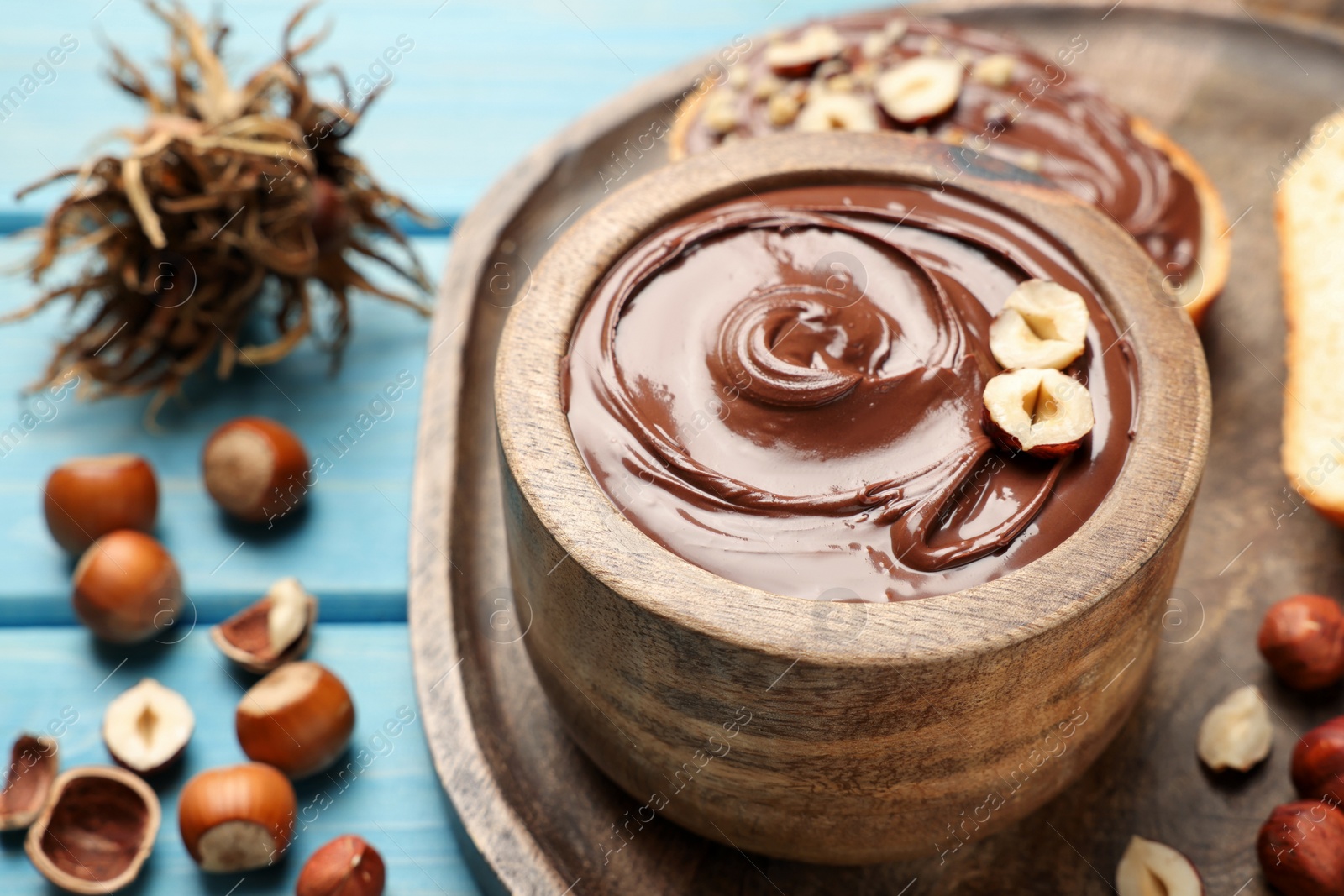 Photo of Bowl of tasty chocolate paste with hazelnuts on light blue wooden table, space for text