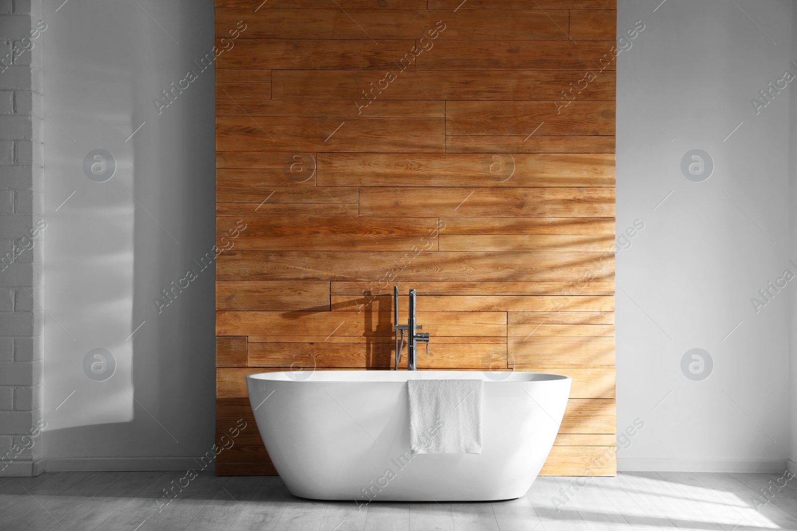 Photo of White bathtub with towel near wooden wall in room