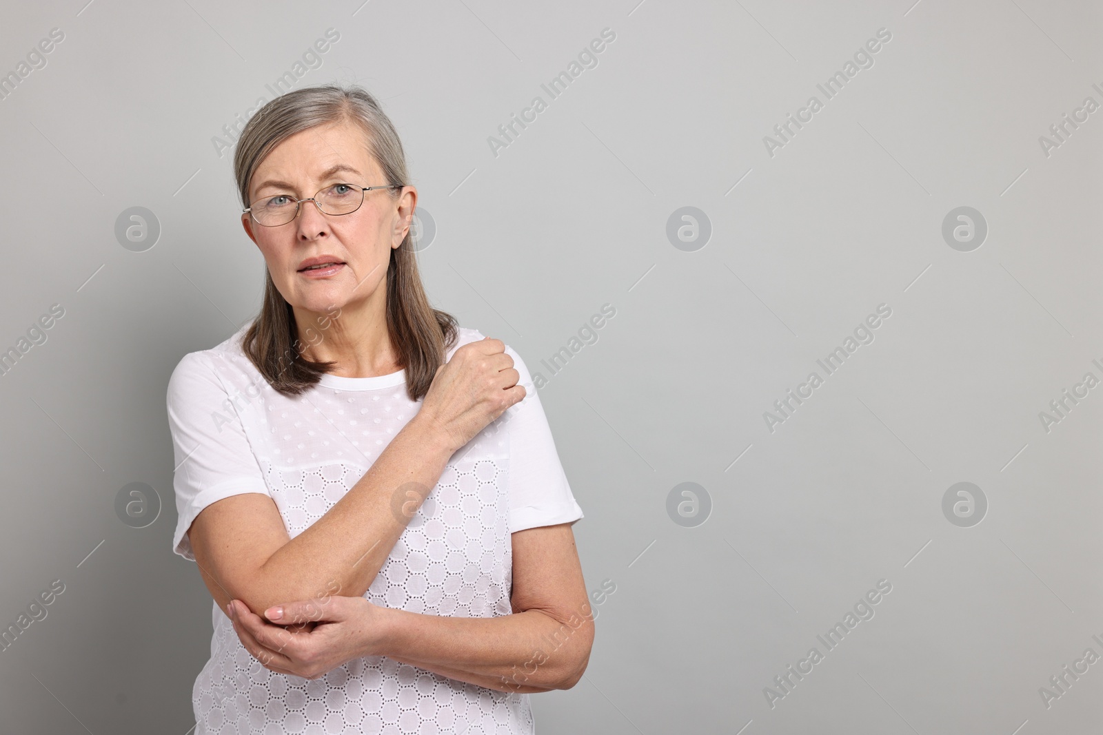 Photo of Arthritis symptoms. Woman suffering from pain in elbow on gray background, space for text