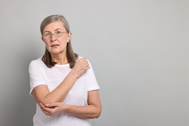 Arthritis symptoms. Woman suffering from pain in elbow on gray background, space for text