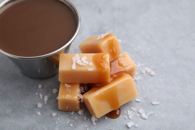 Yummy caramel candies, sauce and sea salt on grey table, closeup. Space for text