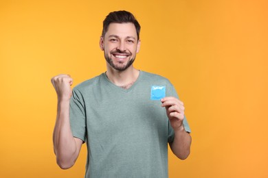 Photo of Happy man holding condom on orange background