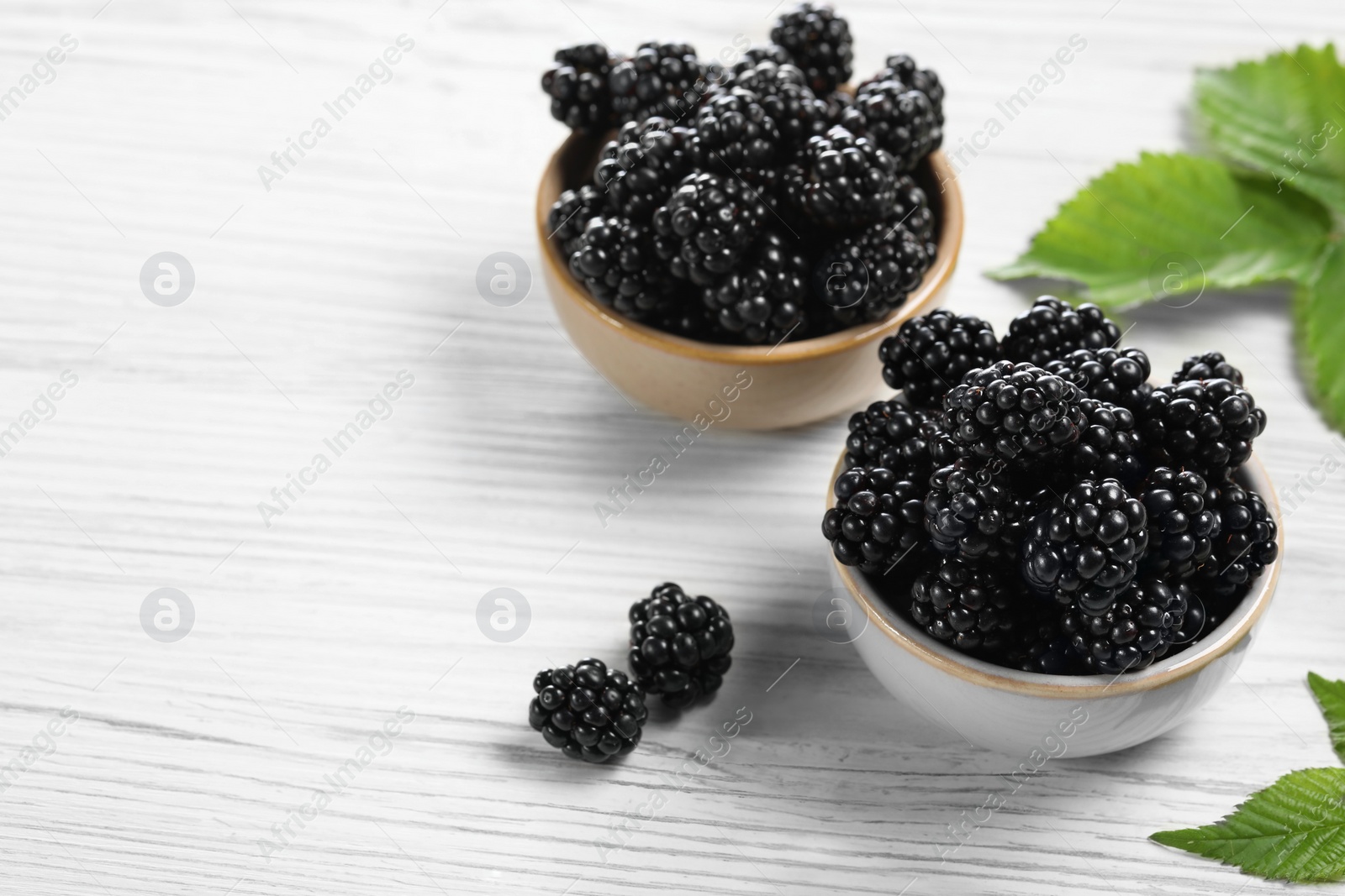 Photo of Ripe blackberries and green leaves on white wooden table, space for text