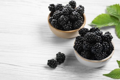 Photo of Ripe blackberries and green leaves on white wooden table, space for text