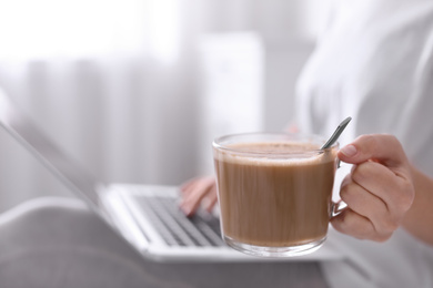 Photo of Woman with cup of morning coffee working on laptop indoors, closeup. Space for text