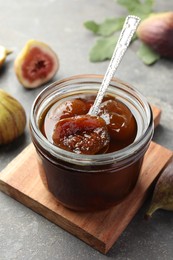 Photo of Jar of tasty sweet fig jam on grey table