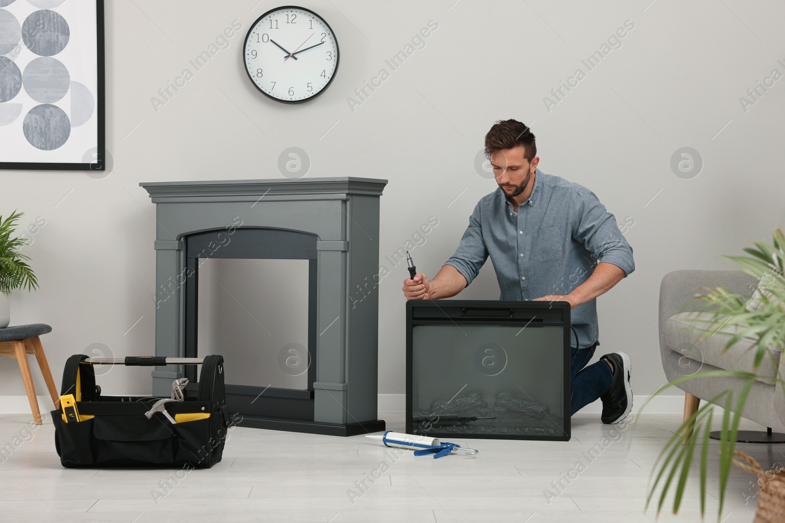 Photo of Man with screwdriver installing electric fireplace near wall in room