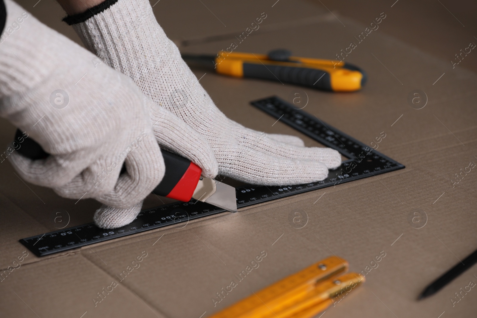 Photo of Worker cutting cardboard with utility knife and ruler, closeup