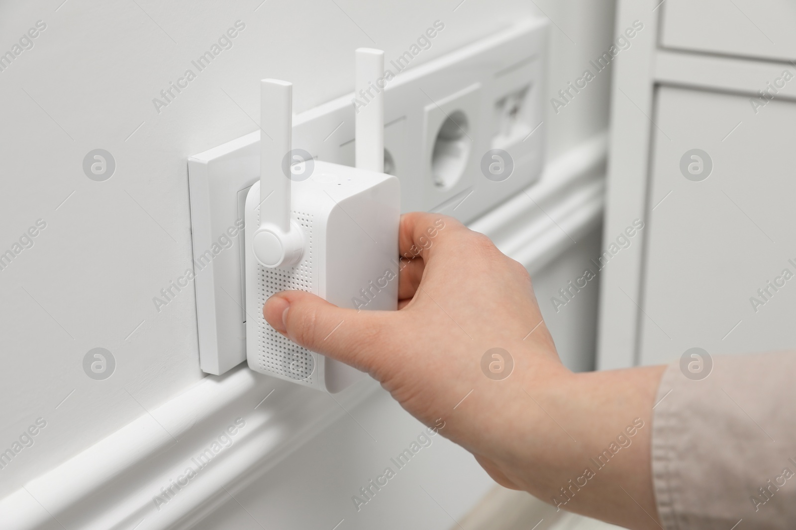 Photo of Woman turning on wireless Wi-Fi repeater indoors, closeup