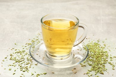 Photo of Aromatic fennel tea in cup and seeds on light grey table, closeup