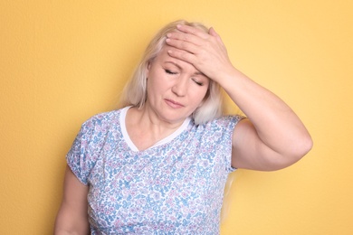 Mature woman suffering from headache on color background