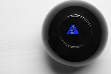 Photo of Magic eight ball with prediction So It Shall Be on white table, closeup. Space for text