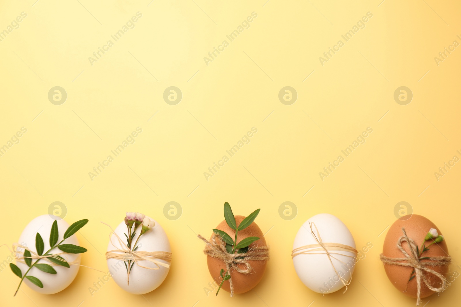 Photo of Festively decorated chicken eggs on yellow background, flat lay with space for text. Happy Easter