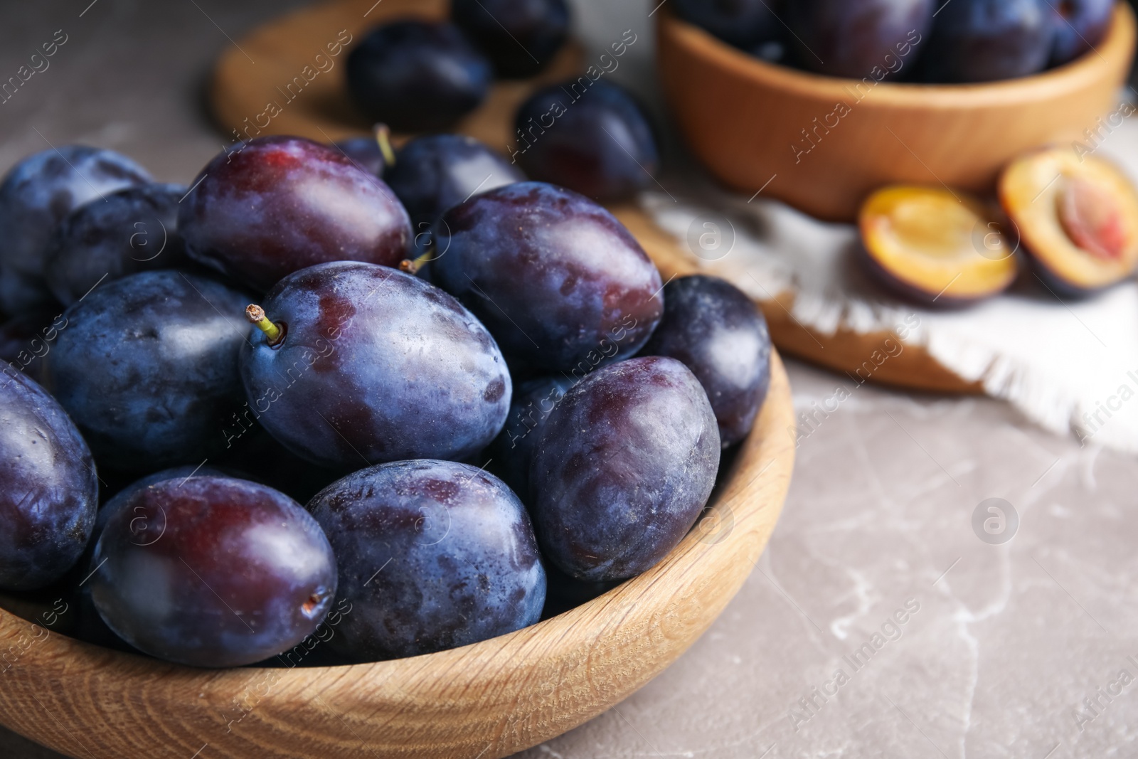 Photo of Delicious ripe plums in wooden bowl on grey marble table, closeup