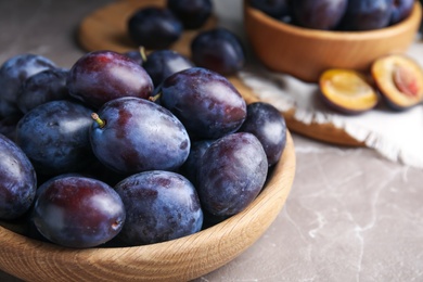 Delicious ripe plums in wooden bowl on grey marble table, closeup