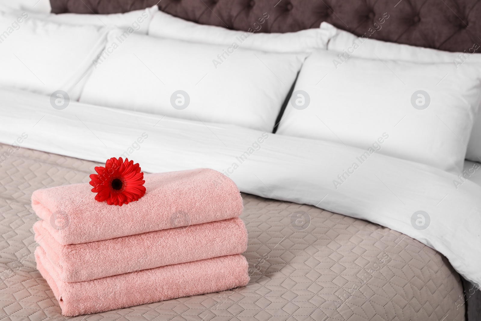 Photo of Stack of fresh towels with flower on blanket in bedroom. Space for text