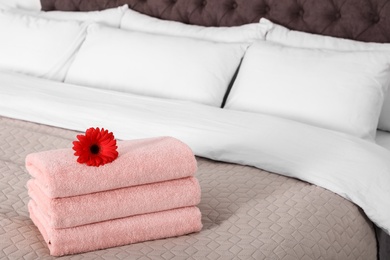 Stack of fresh towels with flower on blanket in bedroom. Space for text