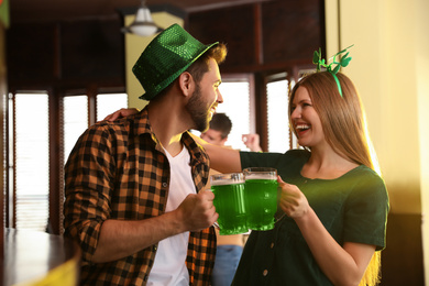 Photo of Young man and woman toasting with green beer in pub. St. Patrick's Day celebration