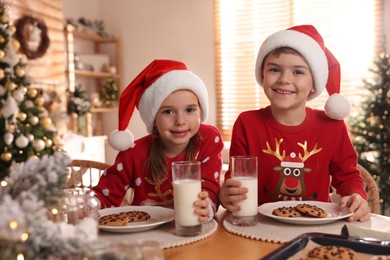 Photo of Cute little children with delicious Christmas cookies and milk at home
