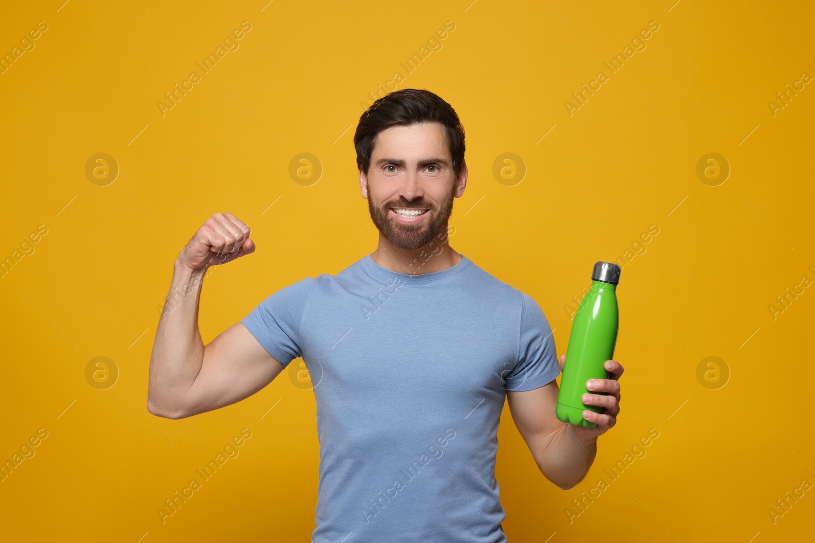 Photo of Man with green thermo bottle showing arm on orange background