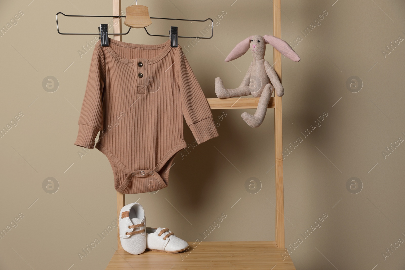 Photo of Baby bodysuit, shoes and toy bunny on chair near beige wall