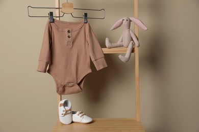 Photo of Baby bodysuit, shoes and toy bunny on chair near beige wall