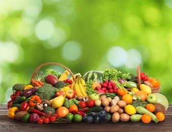 Image of Assortment of fresh organic vegetables and fruits on wooden table against blurred green background 