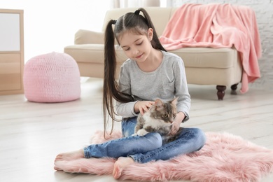 Cute little girl with cat sitting on floor at home