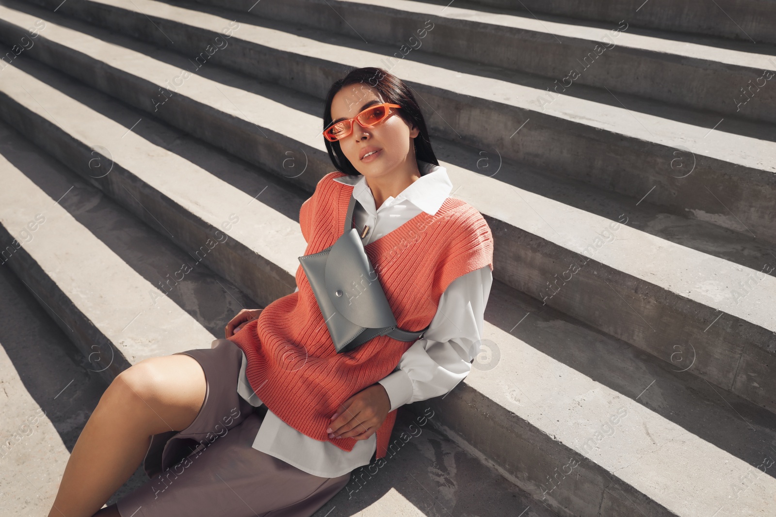 Photo of Beautiful young woman with stylish waist bag on stairs outdoors