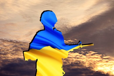 Silhouette of soldier in color of Ukrainian flag with assault rifle against cloudy sky