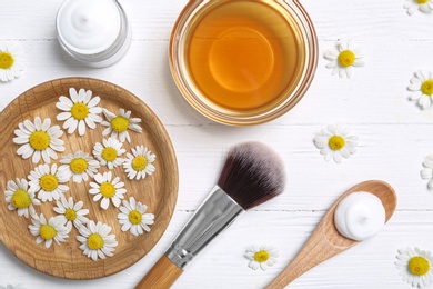 Photo of Flat lay composition with chamomile flowers and cosmetic products on white wooden table