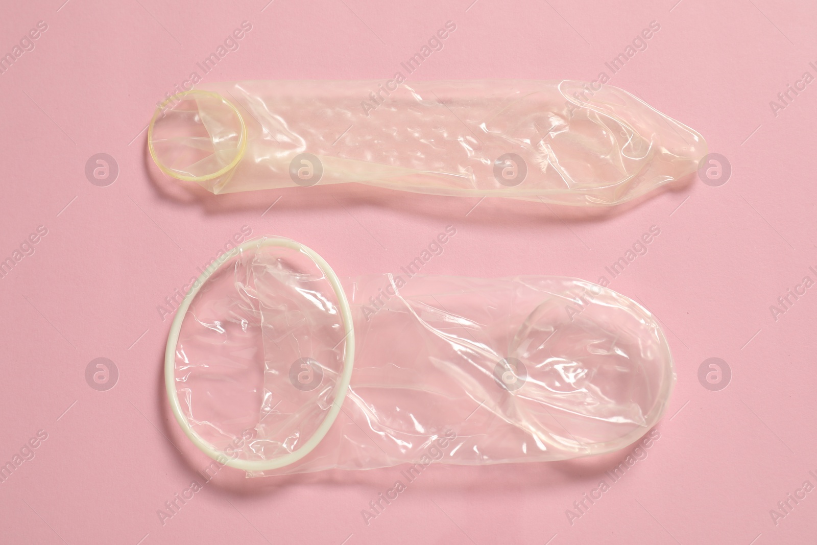 Photo of Unrolled female and male condoms on light pink background, flat lay. Safe sex