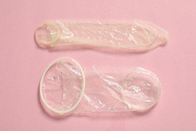 Photo of Unrolled female and male condoms on light pink background, flat lay. Safe sex