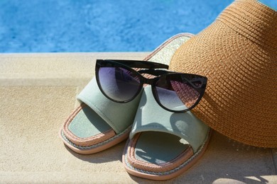 Photo of Stylish sunglasses, visor cap and slippers at poolside on sunny day. Beach accessories