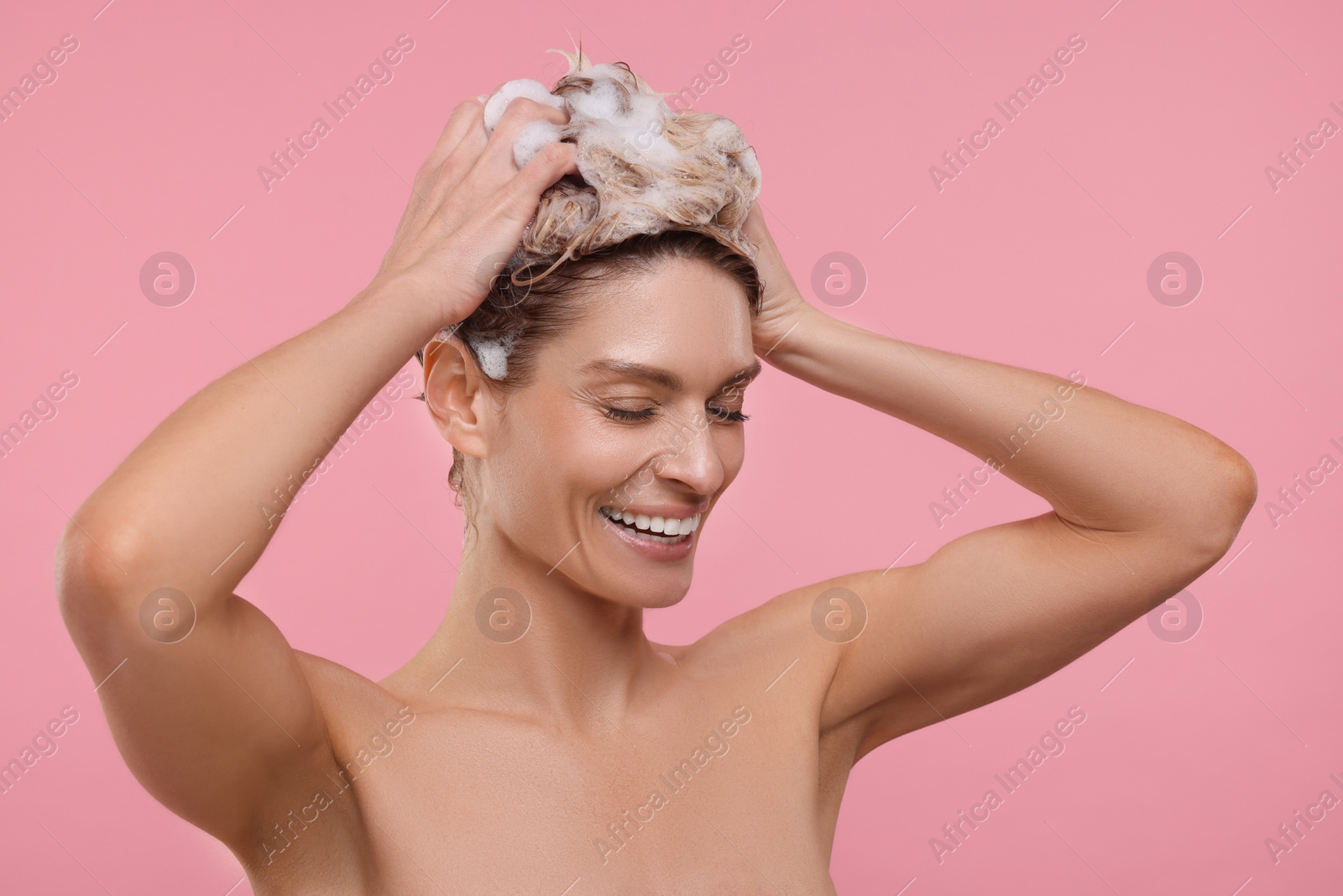 Photo of Beautiful happy woman washing hair on pink background