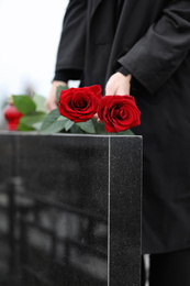 Photo of Woman with red roses near black granite tombstone outdoors, closeup. Funeral ceremony