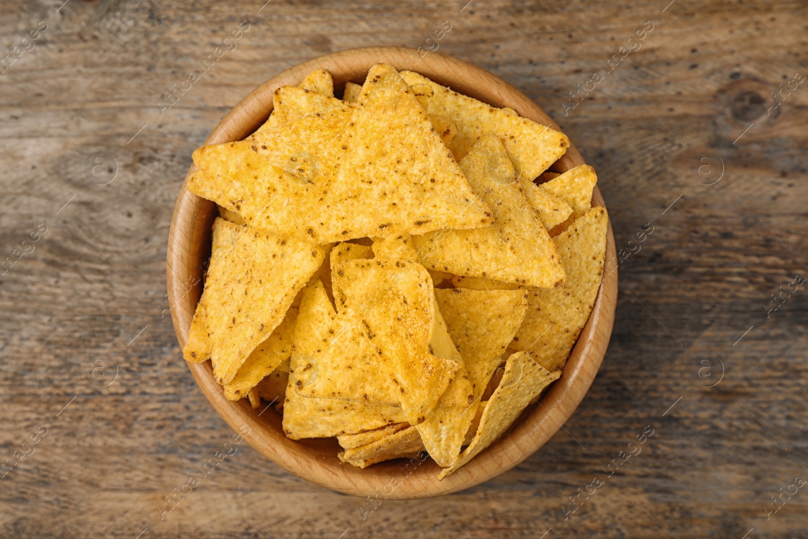 Photo of Bowl with tasty Mexican nachos chips on wooden table, top view