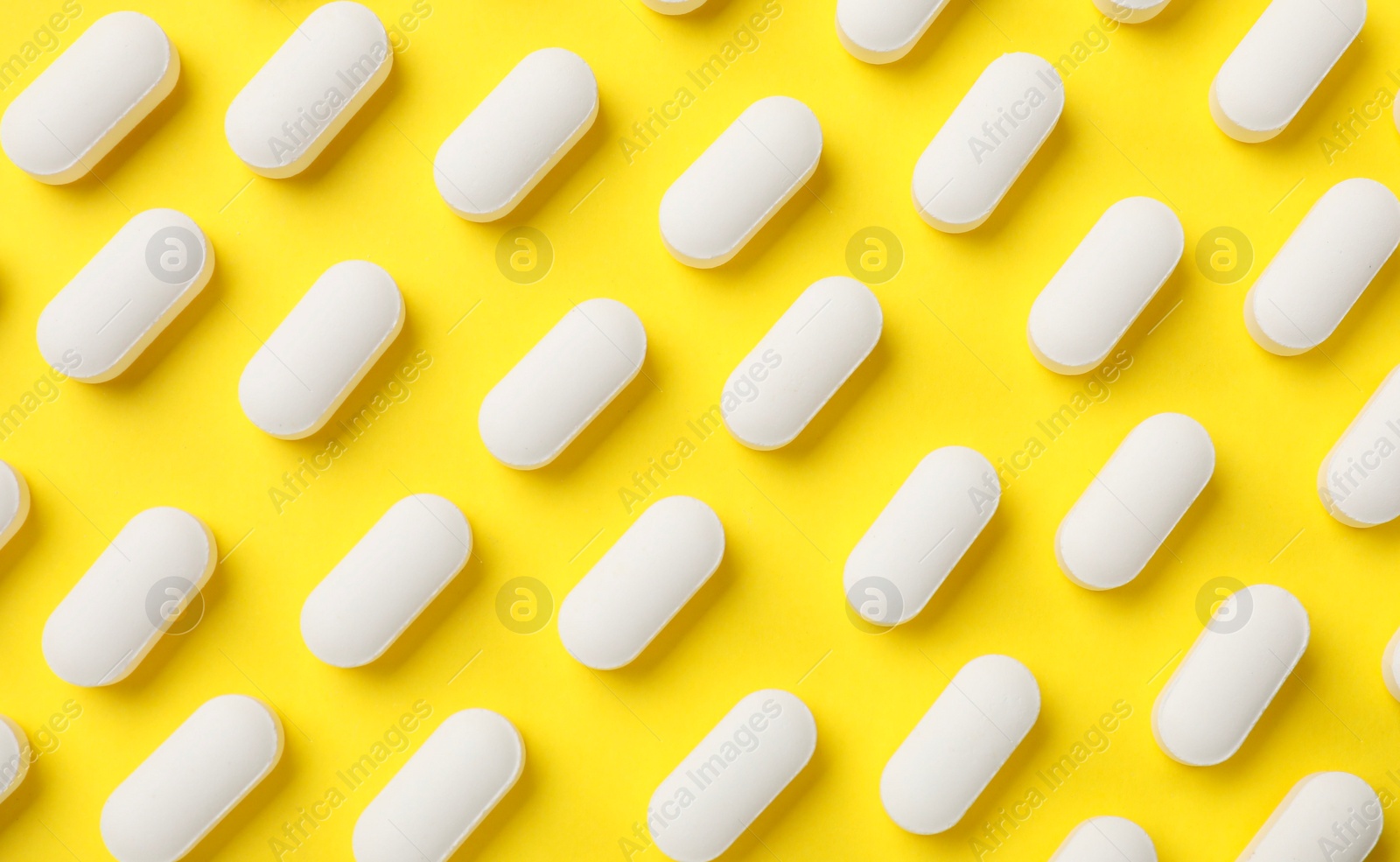 Photo of Vitamin pills on yellow background, flat lay