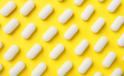 Photo of Vitamin pills on yellow background, flat lay