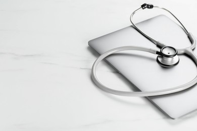 Photo of Modern laptop and stethoscope on white table. Space for text