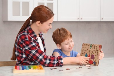 Photo of Happy mother and son playing with math game kit at white marble table in kitchen. Learning mathematics with fun