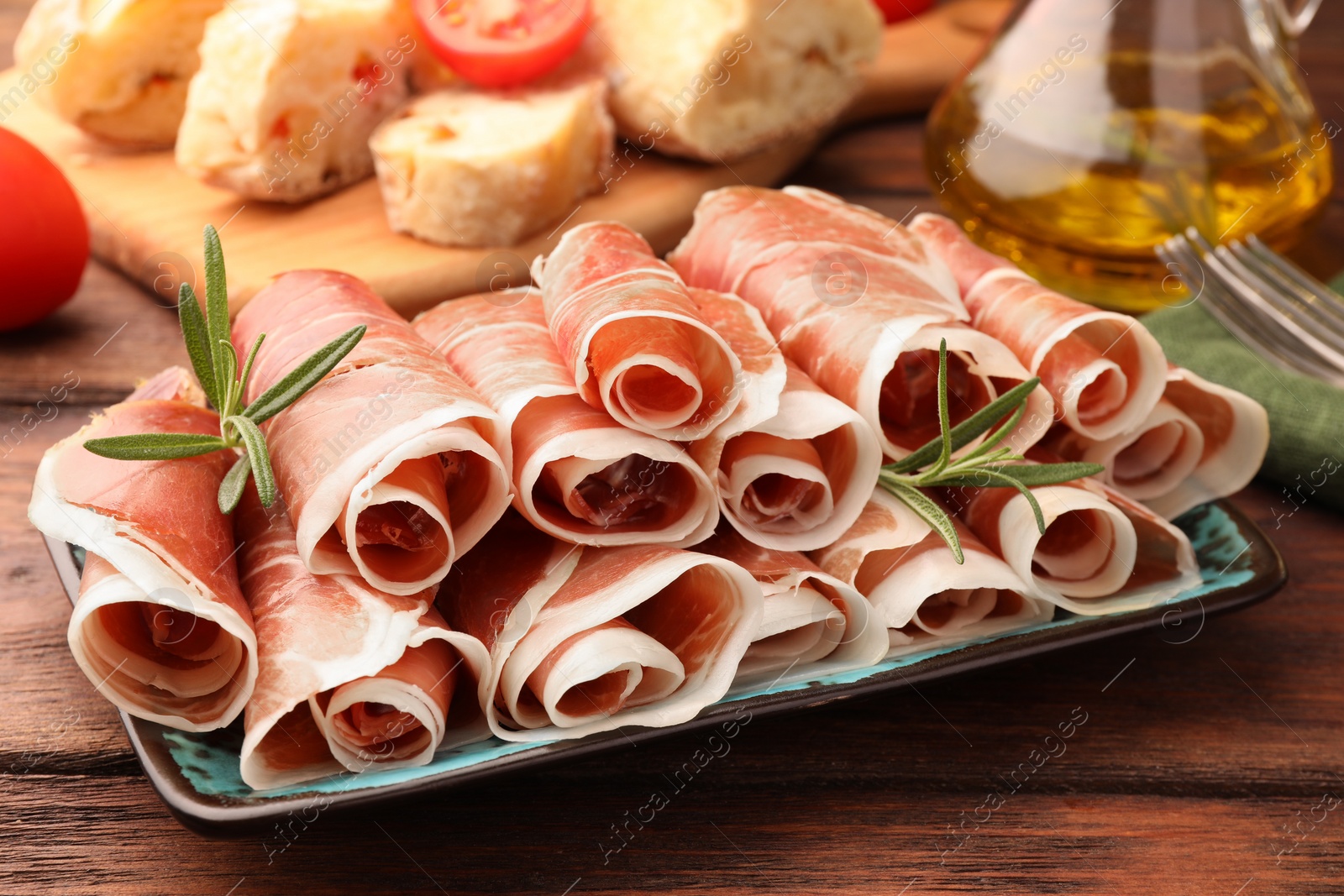 Photo of Rolled slices of delicious jamon with rosemary on wooden table