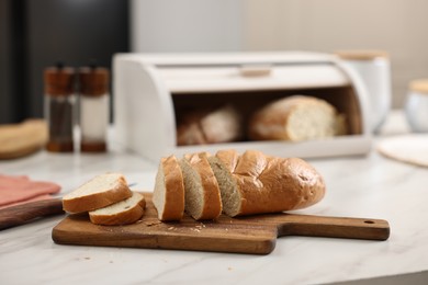 Photo of Wooden bread basket with freshly baked loaves and knife on white marble table in kitchen